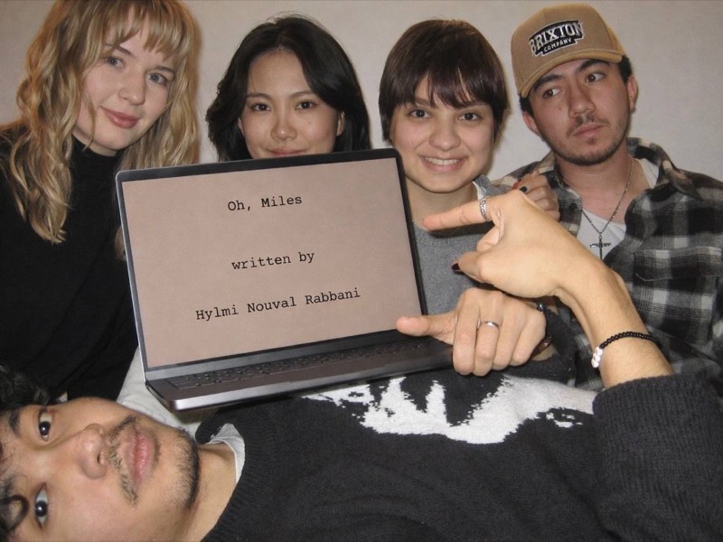 Group gathered around a laptop showing the "Oh, Miles" script