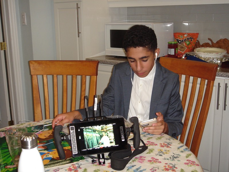 Young man in a blazer at a dining table with a phone and on-set monitor