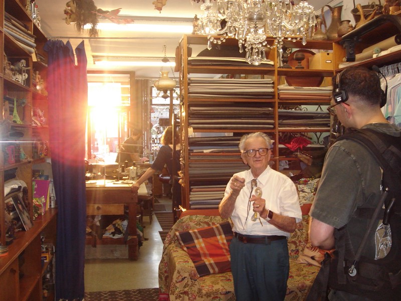 Warm, sunlit interior scene with an older man standing and a crew member beside him