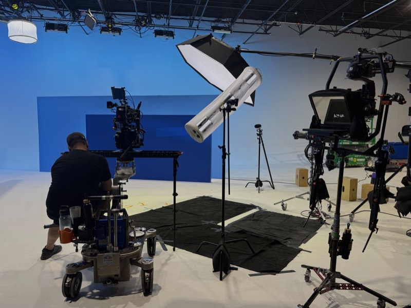 Operator working behind a cinema camera on the studio floor, softbox and monitor rig alongside