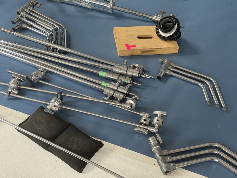 Grip hardware laid out on the floor — C-stand arms, clamps and a matte box ready for the day