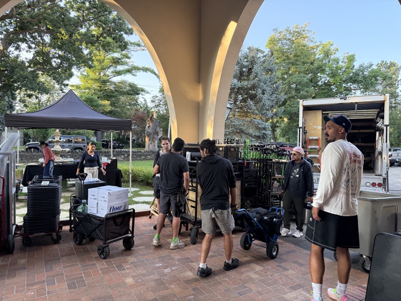 Morning load-in under a stone archway, crew wheeling carts and cases from the truck